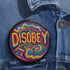 Round black pinback button with neon embroidery-style waves surrounding bold yellow and red "DISOBEY" text.